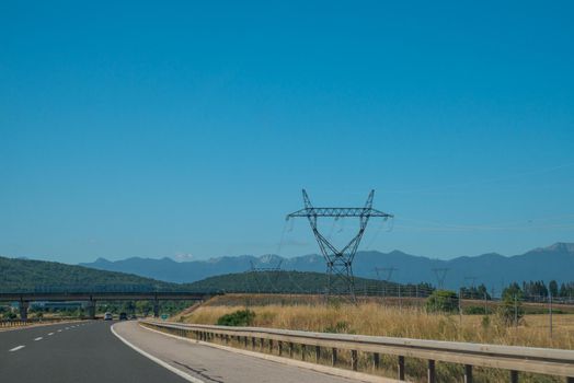 High voltage pole with blue sky, blue sky, trees and grass.