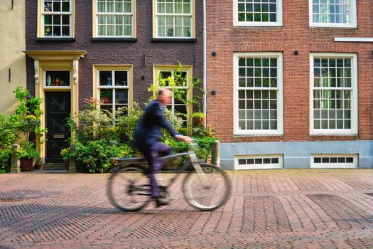 Motion blurred bicycle rider cyclist man on bicycle very popular means of transport in Netherlands in street with old houses of Delft, Netherlands
