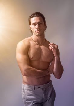 Three quarters shot of handsome shirtless athletic young man in pants, looking at camera in studio shot