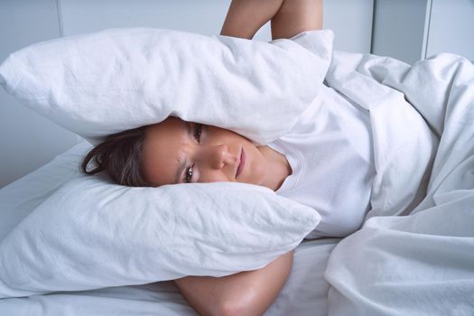 Young woman can't sleep because of noisy neighbours and covering ears with pillows. High quality photo