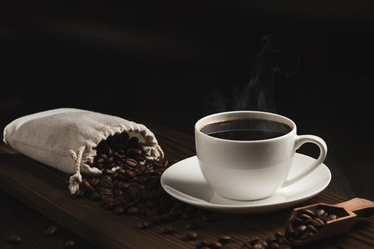 White cup of fresh hot coffee and coffee beans on wooden board on table.