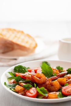 Fresh salad of shrimps, tomatoes, arugula and herbs on a white plate, vertical image.