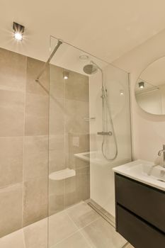 The interior of the bathroom with a shower stall and a ceramic sink under a round mirror