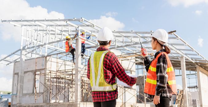 Back two architect and client discussing help create plan with blueprint home building at construction site. Asian engineer foreman worker man and woman meeting talking on drawing paper project