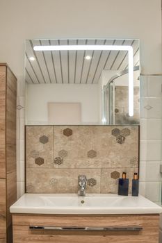 Ceramic sink under the mirror with bathroom accessories and drawers under it in a modern house