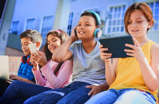 Shot of a diverse group of children having fun with technology outside.