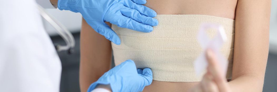 Doctor mammologist examining breast of female patient with elastic bandage closeup. Breast cancer prevention pink ribbon concept