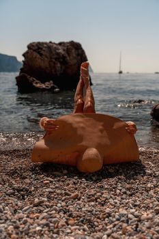 A beautiful middle-aged woman lies on the beach with her feet to the sky, covering her body with a wide-brimmed straw hat. She is sunbathing on the ocean. Vacation, travel, vacation concept