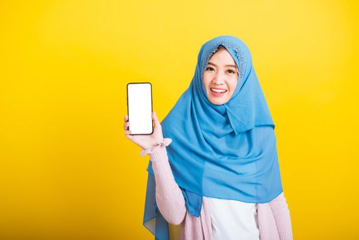 Asian Muslim Arab woman Islam wear veil hijab funny smile she talking on showing blank screen smart mobile phone, studio shot isolated on yellow background