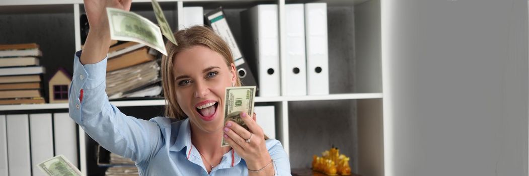 Portrait of happy young woman rolling in money, flying cash in air, abundance of banknotes. Office worker got salary, increase of income. Business, wealth, finance, money fall from sky concept