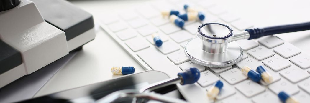 Close-up of medical worker desk, mess on working place, stethoscope tool, scattered pills on keyboard, locked tablet screen. Chaos, messy, slovenliness, medicine, office concept