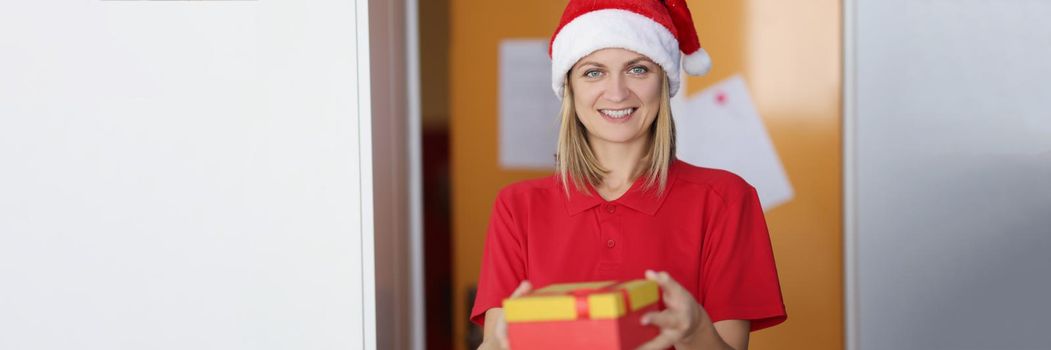 Portrait of woman in festive new year hat delivering parcel to customer, smiling positive worker in special uniform, fast deliver to door. Worldwide shipping, delivery service concept