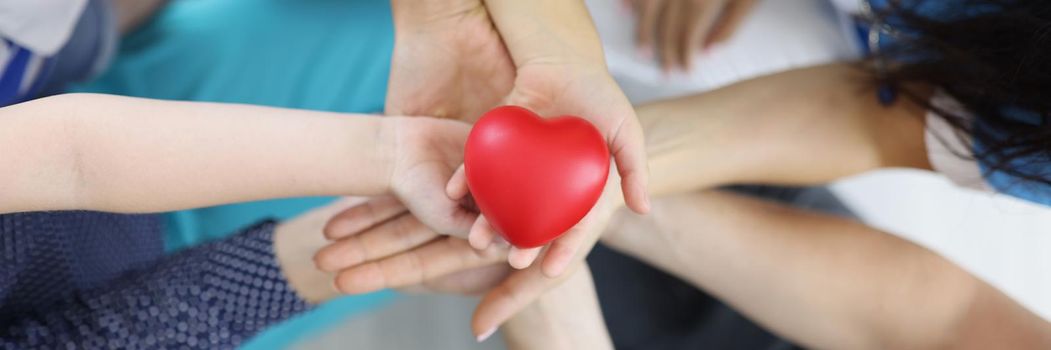 Top view of group of people holding red heart in hands. Adults and children support charity, health insurance, love, international cardiology day, heart health, donation, wellbeing concept