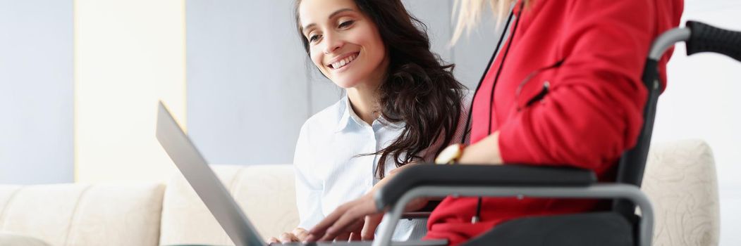Portrait of sisters spend time together watching fun show on laptop, woman in wheelchair hold device on lap. Disabled people, family, sisterhood, pastime, visit concept