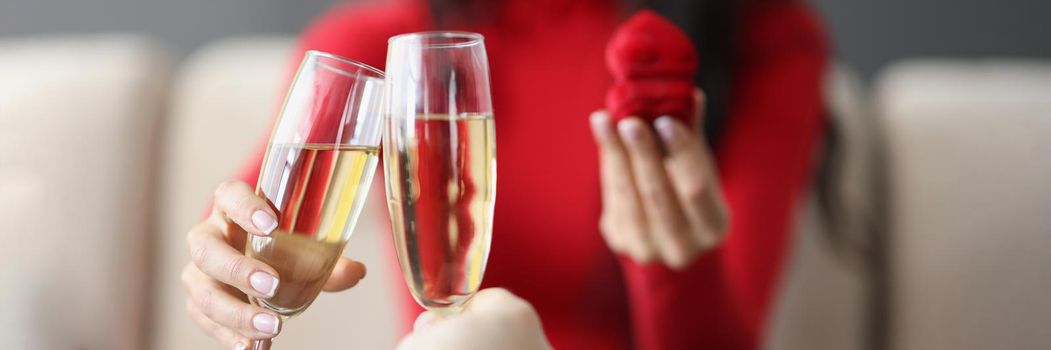 Close-up of couple on romantic dinner, man and woman raise toast with champagne flutes, man proposed to girl, red box with ring. Love, dinner, relationship, spouse, date concept. Blurred background