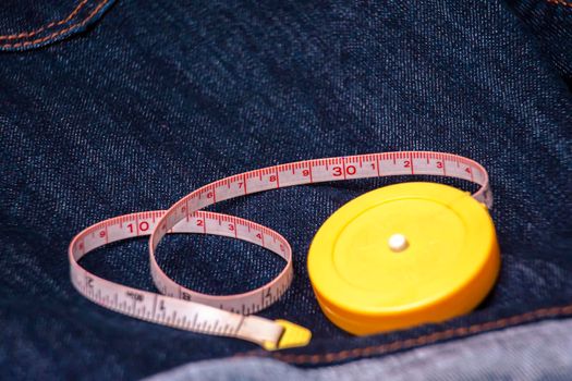 Measuring tape with a yellow color on the denim jeans material with a blue color