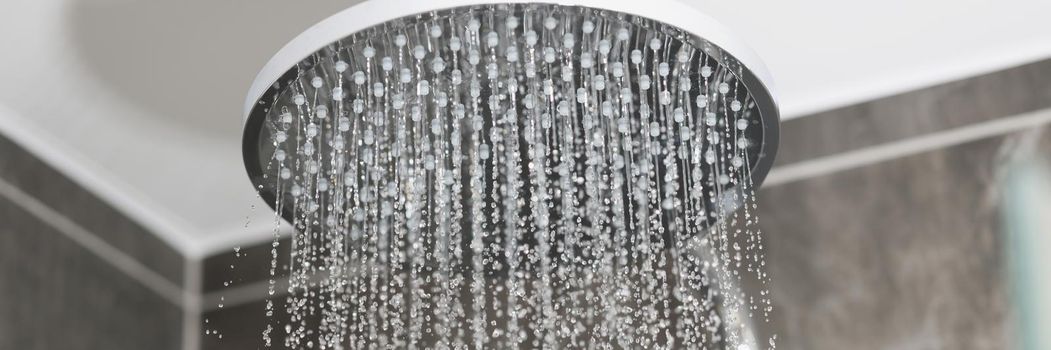 Close-up of water running from shower head and faucet in modern bathroom, water drops splashing, water stream. Shower turned on, nobody washing. Water saving, renovation concept