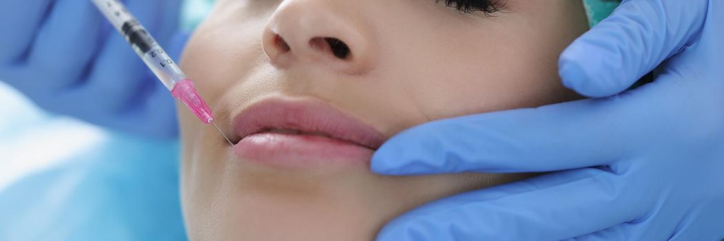 Portrait of young woman gets injection of botox in her lips, cosmetologist using syringe with special liquid. Cosmetology, beauty treatment, plastic surgery, clinic concept