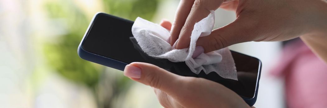 Close-up of cleaning mobile phone screen with wet wipe, antibacterial and disinfecting wipe. Protective glass on smartphone screen. Technology, cleaning, prevent virus concept. Blurred background