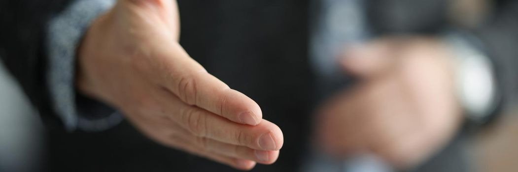 Close-up of man extending hand for handshake, greeting, offering cooperation, welcoming at job interview. Gesture of confirm agreement, successful negotiation concept. Blurred background