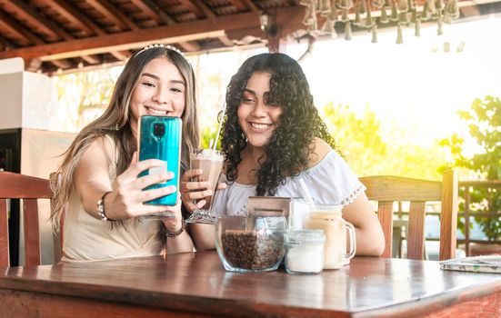 Two girls taking a selfie and drinking coffee, two girls friends in a coffee shop taking a selfie