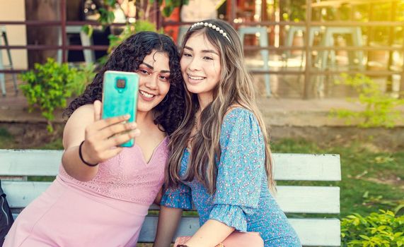 Two pretty girls sitting on a bench taking a selfie, girls smiling and taking a selfie, sisterly friendship concept