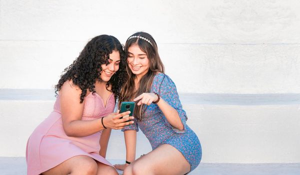 Two girls pointing at her cell phone, Girl showing her smartphone to her friend, girl checking her cell phone with her friend