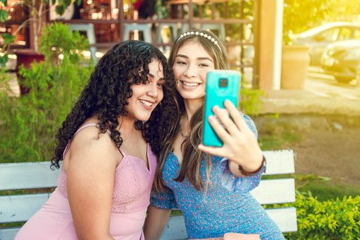 Two pretty girls sitting on a bench taking a selfie, girls smiling and taking a selfie, sisterly friendship concept