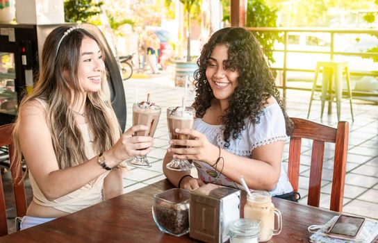 Two girls having a milkshake, two girl friends in a cafe, two girls toasting in a cafe