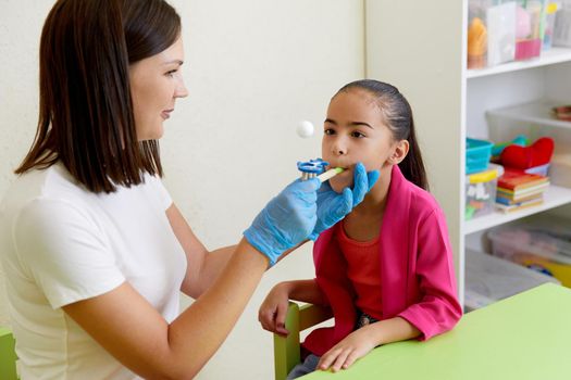 Speech therapist working with little girl in office training correct pronunciation