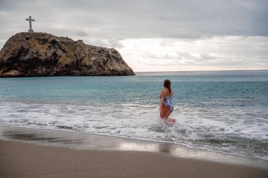 A plump woman in a bathing suit enters the water during the surf. Alone on the beach, Gray sky in the clouds, swimming in winter