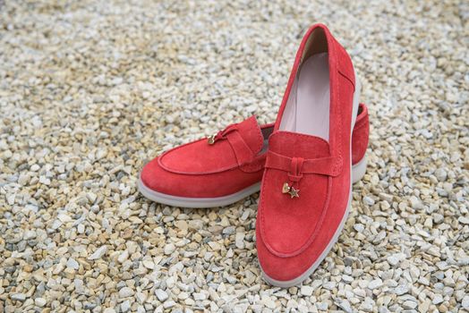 Woman's red stylish suede loafer shoes on the stone background. Pair of trendy female loafers shoes, outdoors.