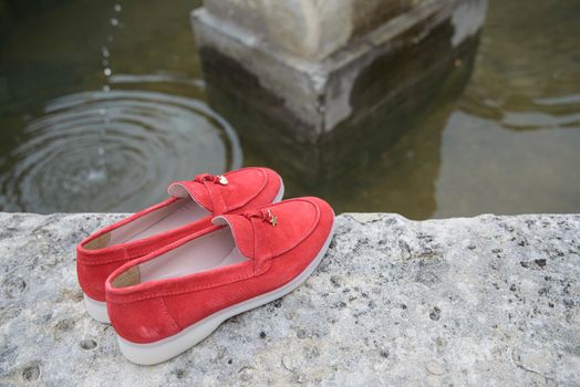 Woman's red stylish suede loafer shoes on the stone background. Pair of trendy female loafers shoes, outdoors.