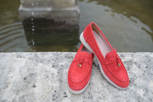 Woman's red stylish suede loafer shoes on the stone background. Pair of trendy female loafers shoes, outdoors.