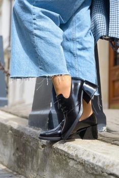 Women's leather boots close-up. The girl walks in black shiny oxford style shoes.