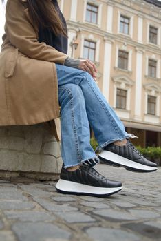 Stylish young girl posing. She is wearing a beige coat, jeans and stylish leather sports shoes.