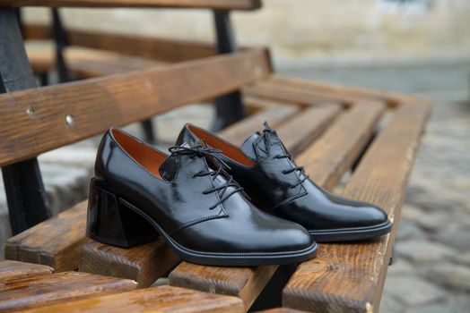 Women's leather boots close-up. black shiny oxford style shoes on a wooden bench.