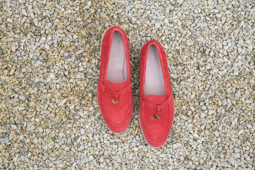 Woman's red stylish suede loafer shoes on the stone background. Pair of trendy female loafers shoes, outdoors.