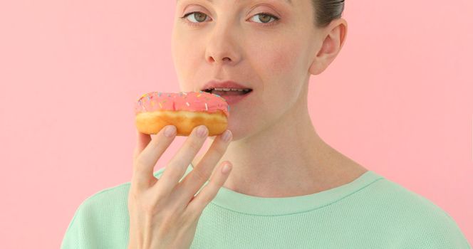 Female mouth bites a loaf. Close-up woman eating a donut , delicious, sweet, sweet tooth at pink background