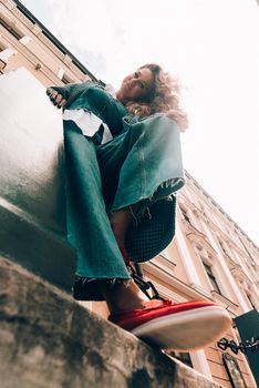 Woman in a red stylish suede loafer shoes, blue jeanse, white shirt and trendy checkered coat. Pair of trendy female loafers shoes, outdoors