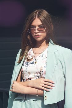 Fashion portrait of young woman wearing sunglasses, top and blue suit. Young beautiful happy model posing on the dark background.