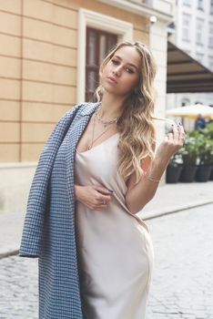 Fashionable young woman with blond hair dressed in beige dress and checkered coat posing. Street style.