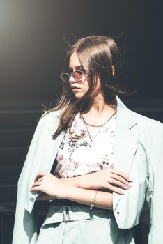 Fashion portrait of young woman wearing sunglasses, top and blue suit. Young beautiful happy model posing on the dark background.