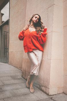 Portrait of fashionable blond women in orange sweater, beige dress and stylish suede loafer shoes posing in the street