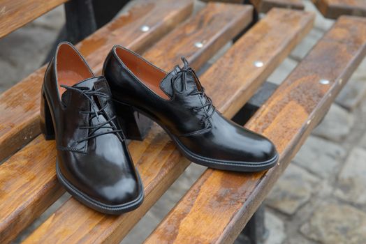 Women's leather boots close-up. black shiny oxford style shoes on a wooden bench.