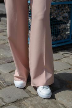 Stylish woman in fashion white sneakers shoes and beige trousers walks around the city. Close-up.