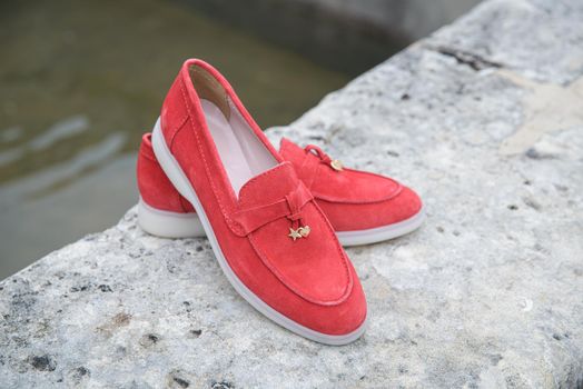 Woman's red stylish suede loafer shoes on the stone background. Pair of trendy female loafers shoes, outdoors.