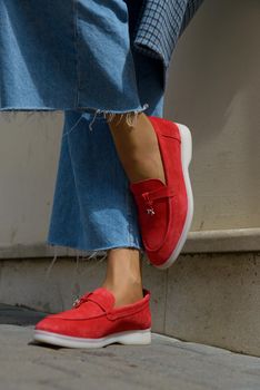 Woman in a red stylish suede loafer shoes, blue jeanse, white shirt and trendy checkered coat. Pair of trendy female loafers shoes, outdoors