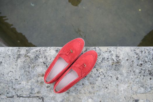 Woman's red stylish suede loafer shoes on the stone background. Pair of trendy female loafers shoes, outdoors.