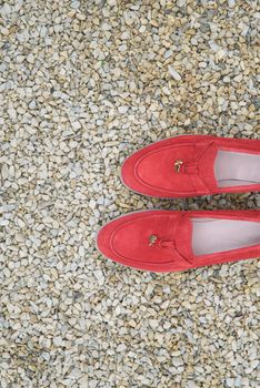 Woman's red stylish suede loafer shoes on the stone background. Pair of trendy female loafers shoes, outdoors.